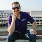 A cool guy wearing shades, smiling while enjoying Cannabis Pharmacy CBD Gummies, 50mg assorted flavors, 30-count.